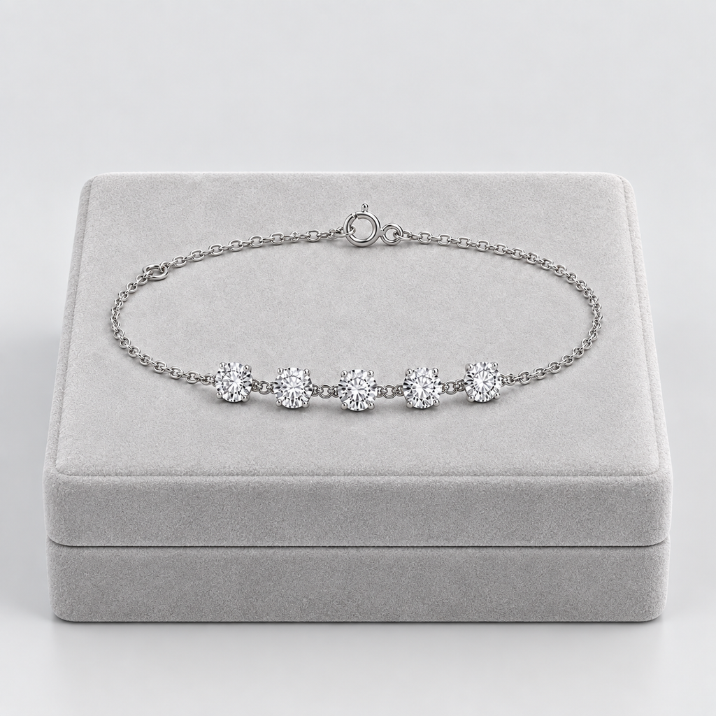 A silver chain bracelet with five round-cut clear gemstones, displayed on a light gray velvet jewelry box against a light gray background.
