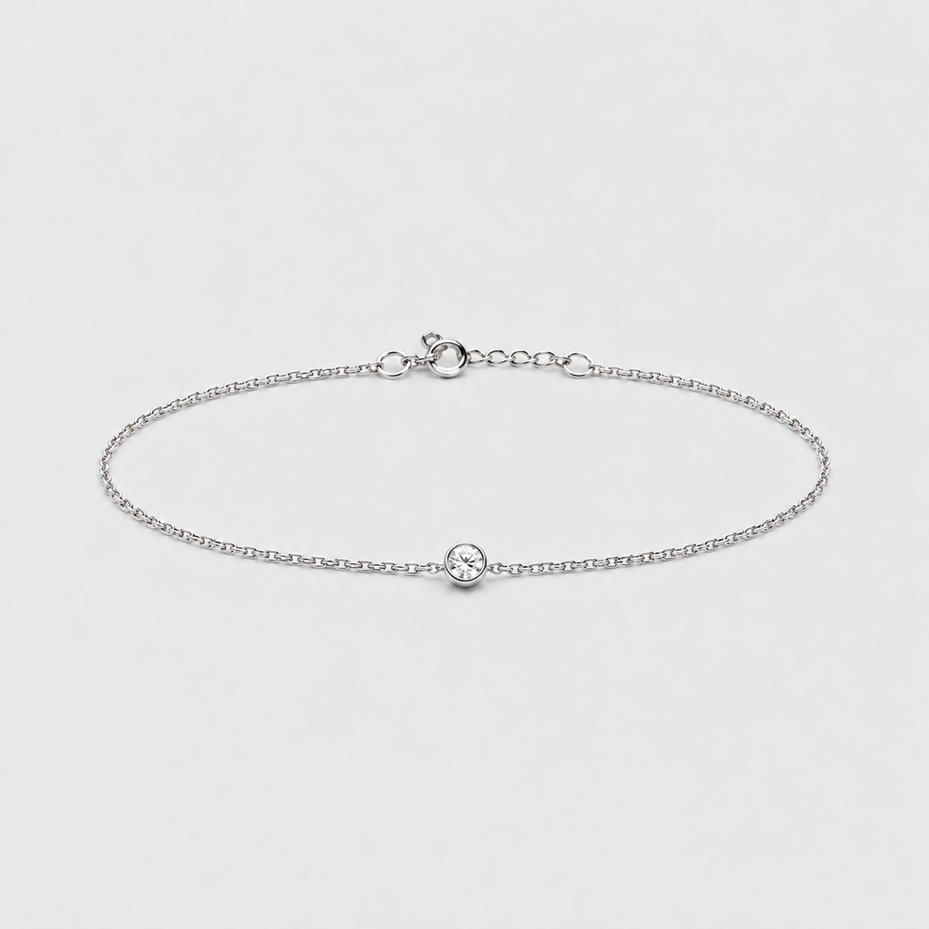 A delicate silver chain anklet with a small central oval charm, displayed on a clean light gray background.