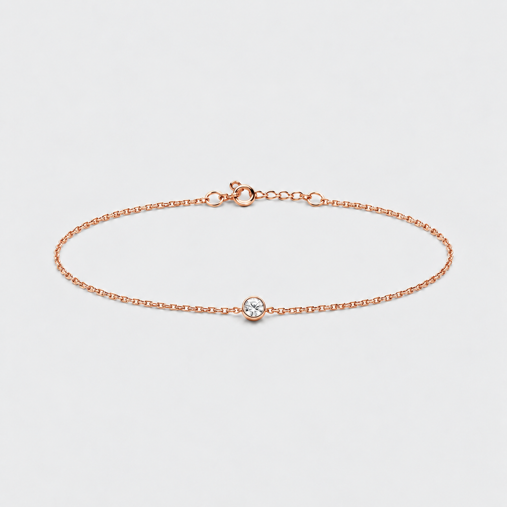 A delicate rose gold chain bracelet with a small bezel-set clear gemstone at the center, displayed on a clean light gray background.