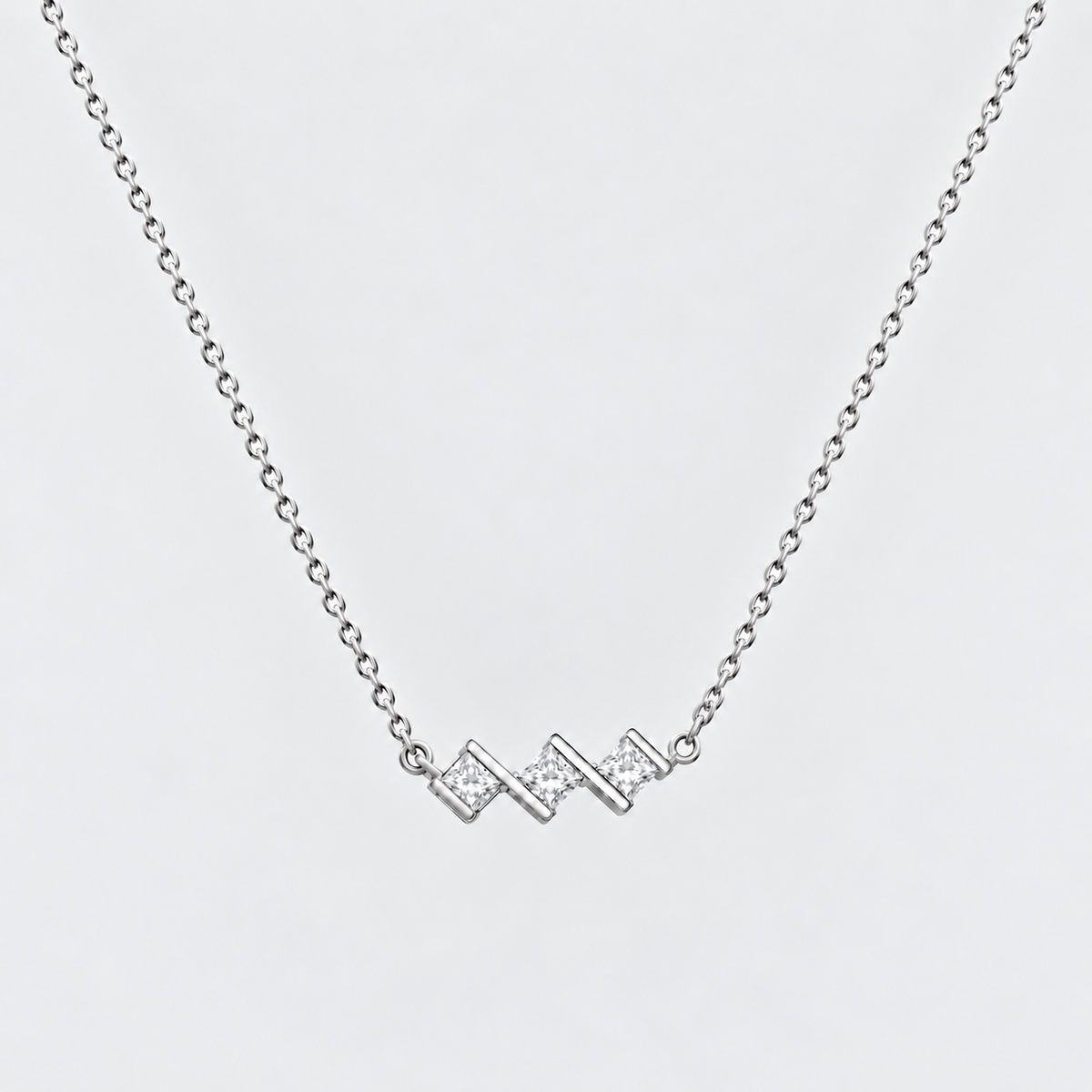 A silver chain necklace featuring a small zigzag pendant paved with clear stones, shown against a light gray background.