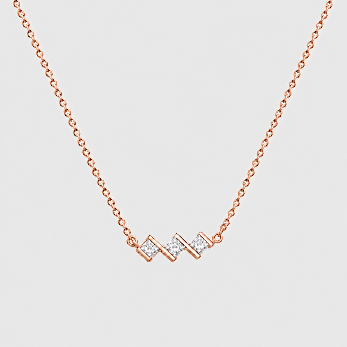 A delicate rose gold chain necklace featuring a modern zigzag pendant adorned with small clear pavé stones, set against a solid light gray background.