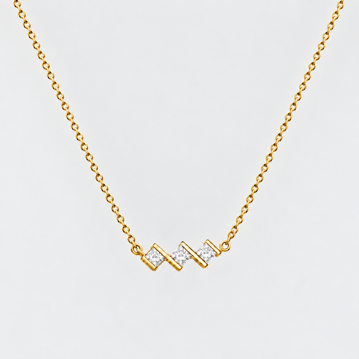 A gold chain necklace with a zigzag pendant featuring small clear stones, shown against a light gray background.
