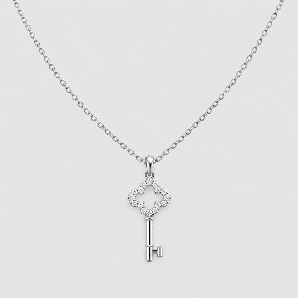 A silver key-shaped pendant necklace adorned with small clear stones, suspended from a delicate silver chain against a light gray background.