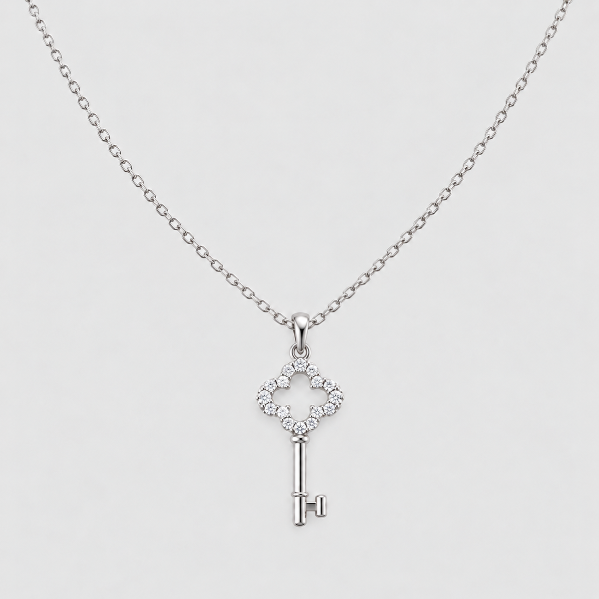 A silver key-shaped pendant necklace adorned with small clear stones, suspended from a delicate silver chain against a light gray background.