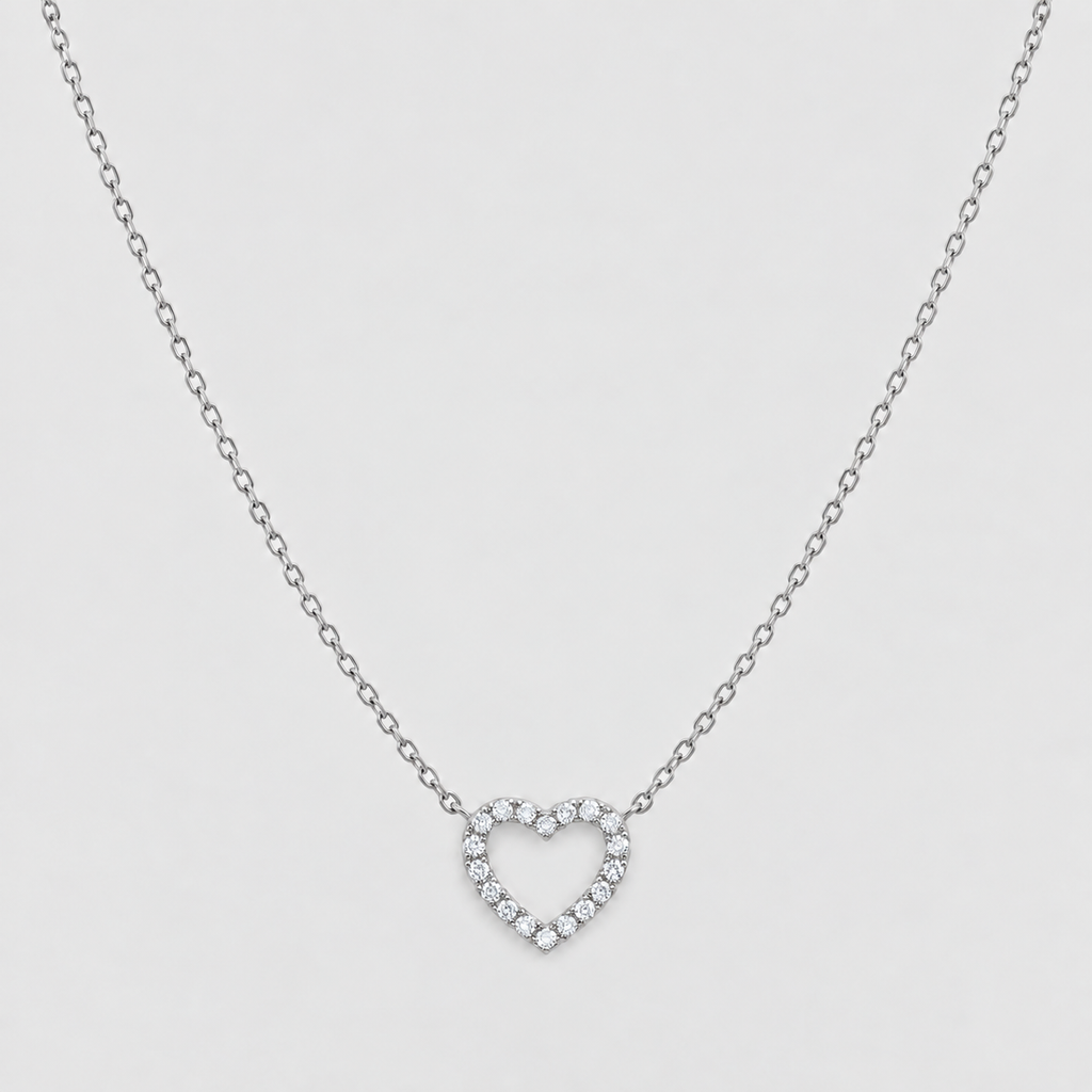 A delicate silver chain necklace featuring a small open heart-shaped pendant encrusted with clear stones, presented on a light gray background.
