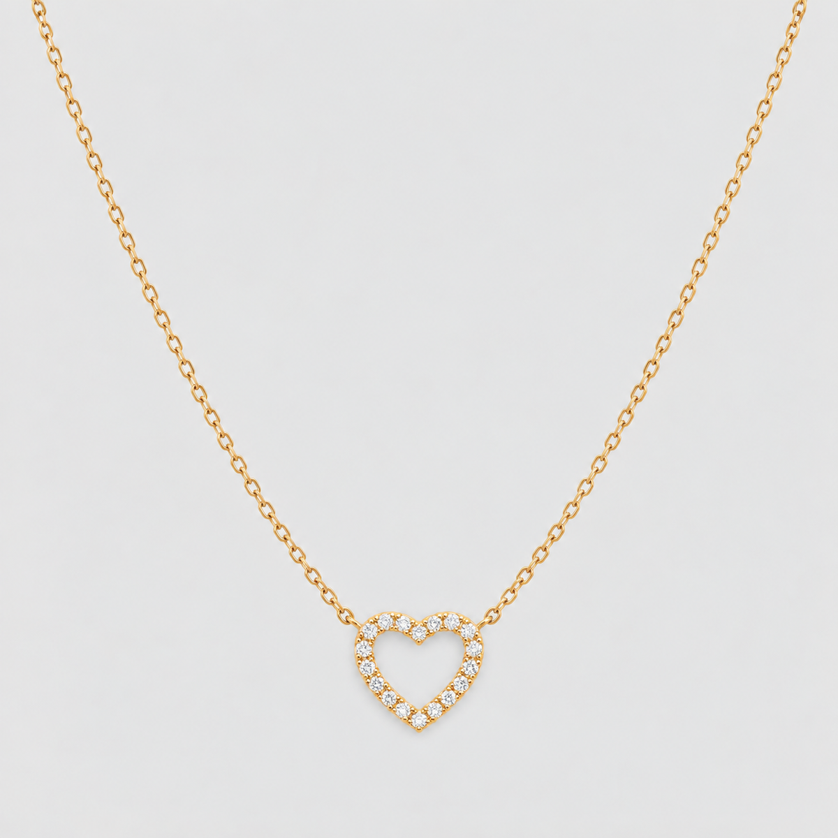 A delicate gold chain necklace featuring an open heart pendant encrusted with small clear stones, displayed against a clean, light gray background.