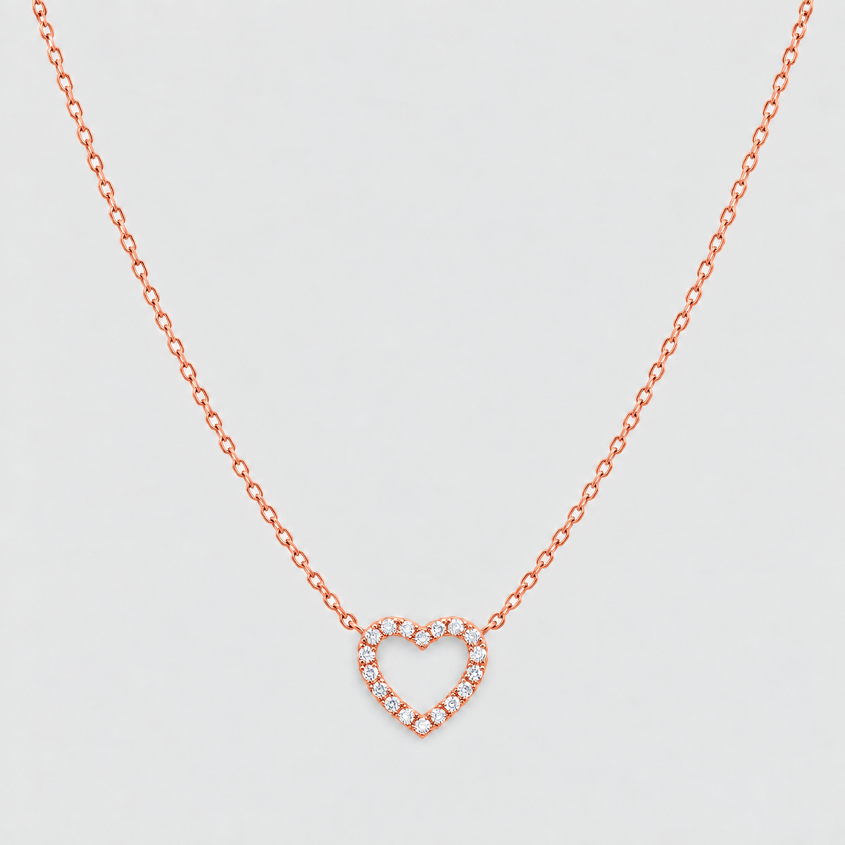 A delicate rose gold chain necklace featuring a heart-shaped pendant paved with small clear stones, displayed against a clean, light gray background.