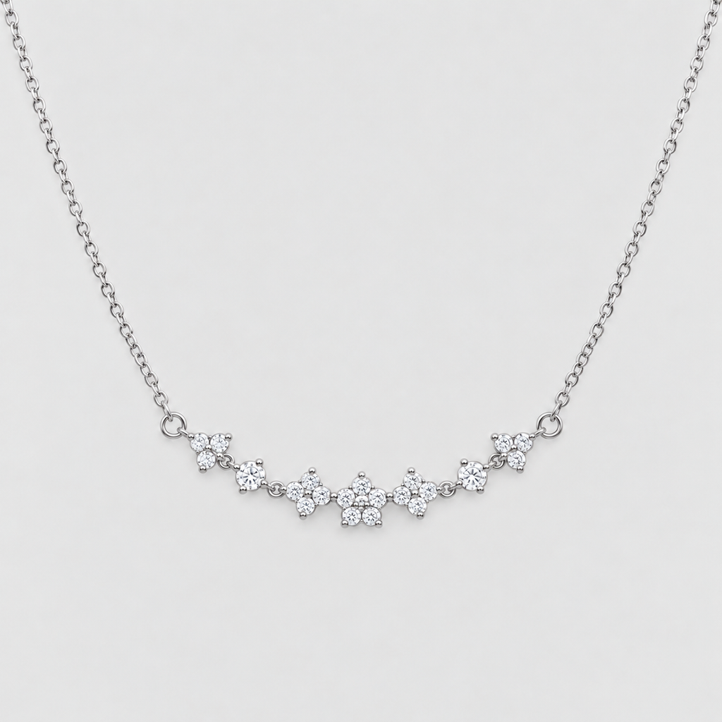 A delicate silver chain necklace featuring a curved bar of small, clear gemstone clusters set in silver, displayed against a light gray background.