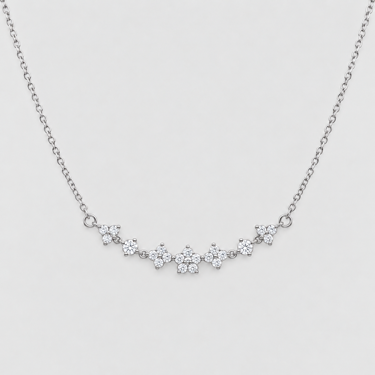 A delicate silver chain necklace featuring a curved bar of small, clear gemstone clusters set in silver, displayed against a light gray background.