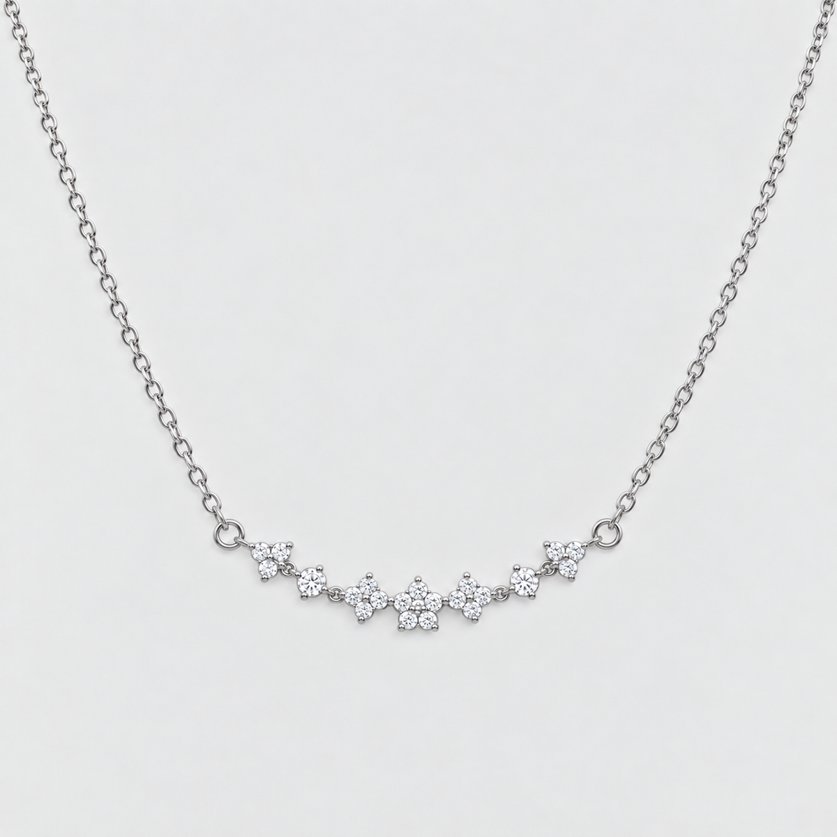 A delicate silver chain necklace featuring a curved bar of small flower-shaped clusters set with clear stones, displayed against a light gray background.