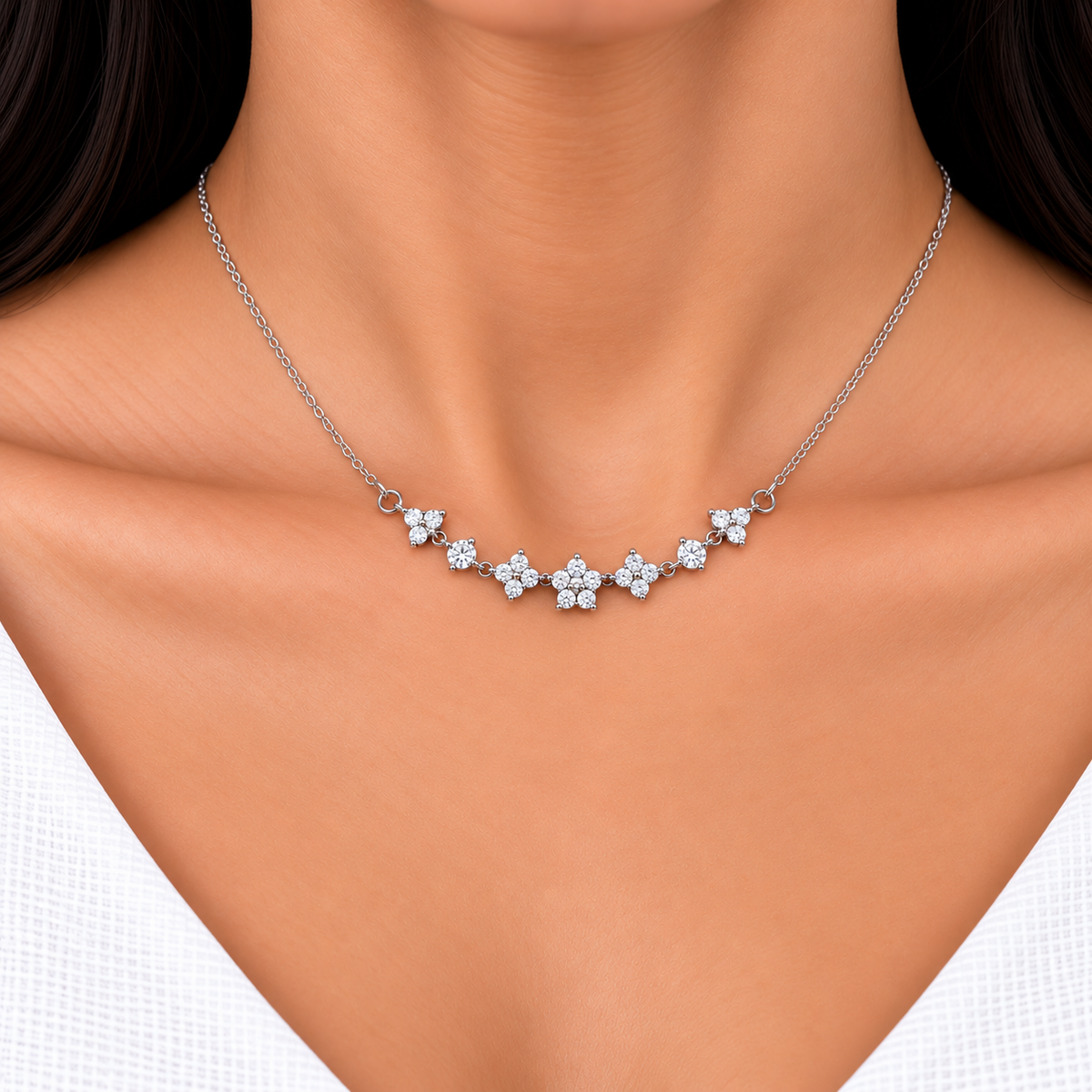 A close-up of a delicate silver necklace with a row of small flower clusters set with clear stones, worn on a model's neck.