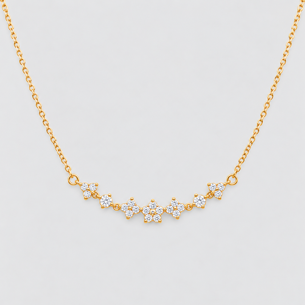 A delicate gold chain necklace featuring a curved bar of small flower-shaped clusters set with clear stones, displayed against a light gray background.