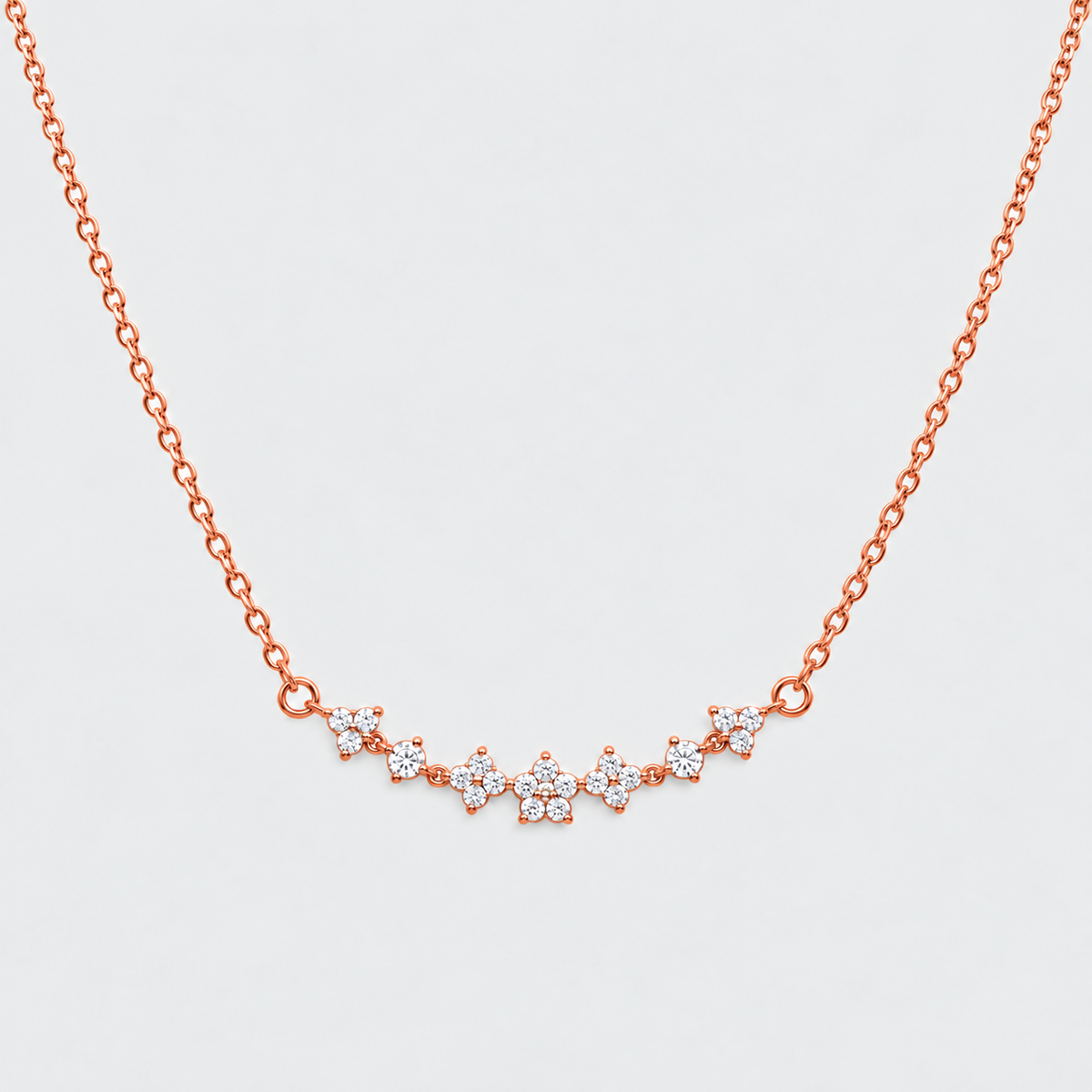 A delicate rose gold chain necklace featuring a curved bar of small star-shaped clusters of clear stones, set against a light gray background.