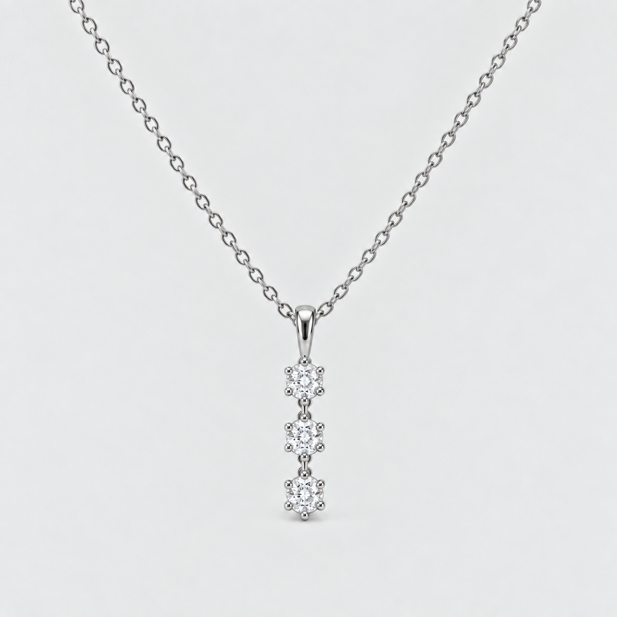 A silver chain necklace with a vertical pendant featuring four small clear gemstones in a prong setting, shown against a light gray background.