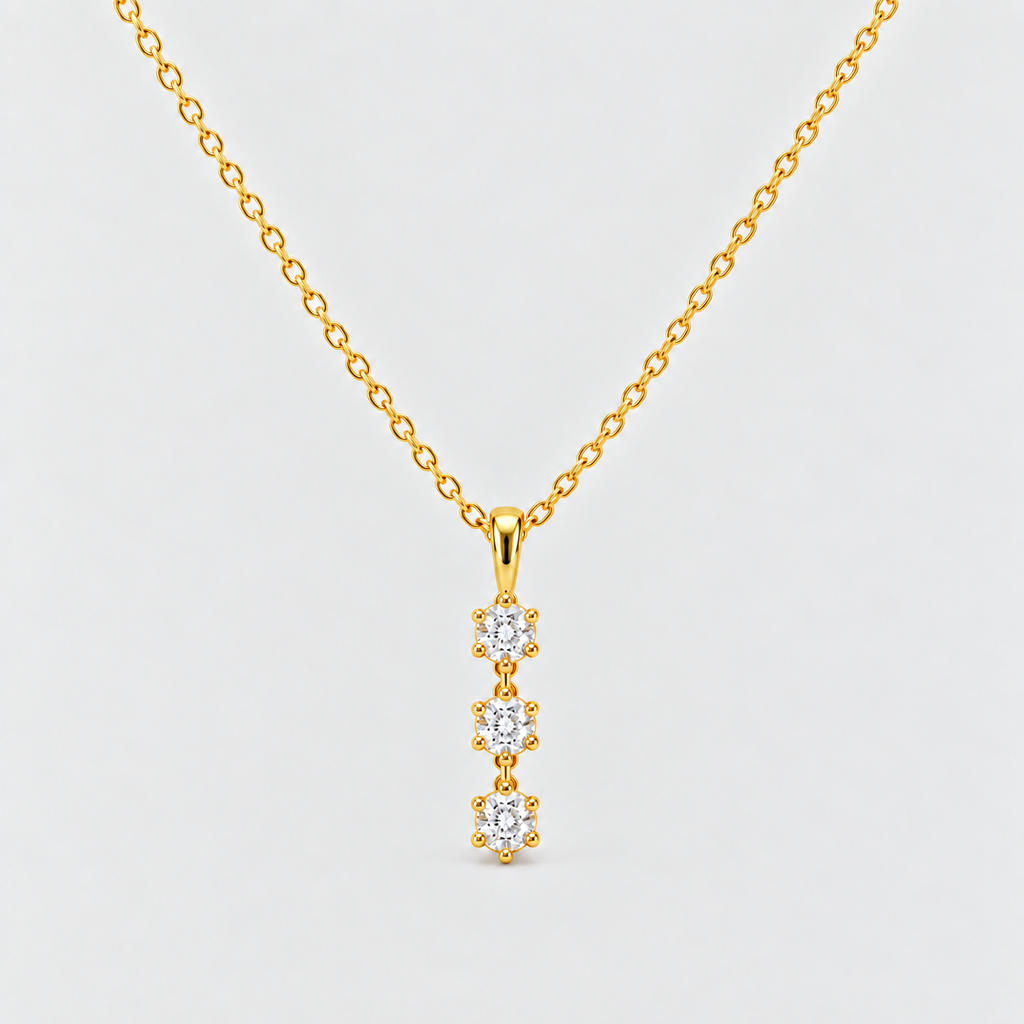 A gold chain necklace with a vertical pendant featuring three small clear gemstones in gold settings, shown against a light gray background.