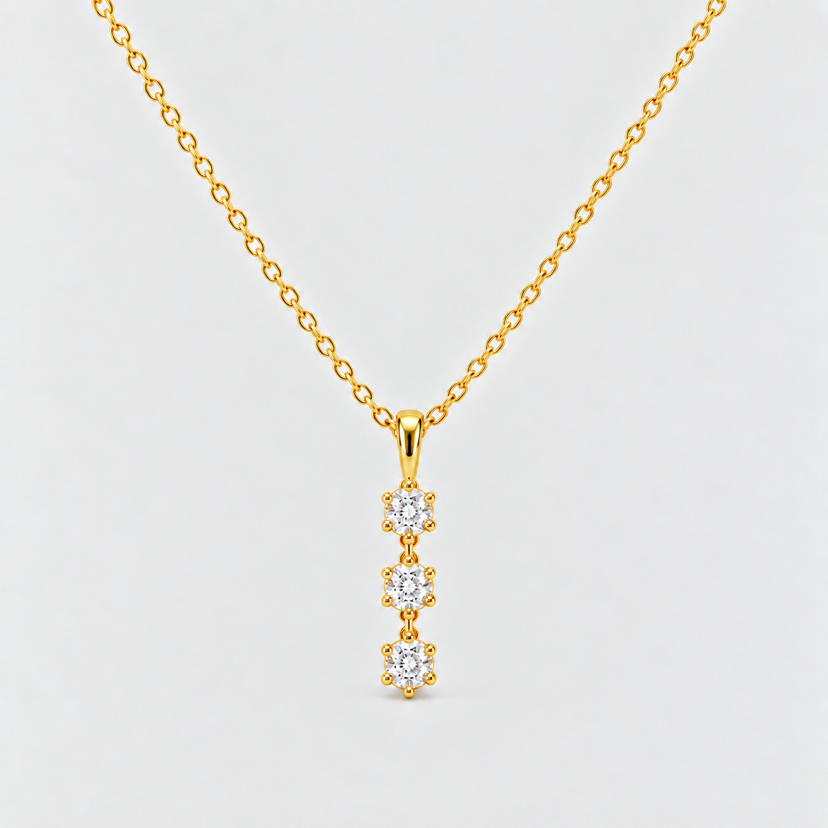 A gold chain necklace with a vertical pendant featuring three small clear gemstones in gold settings, shown against a light gray background.
