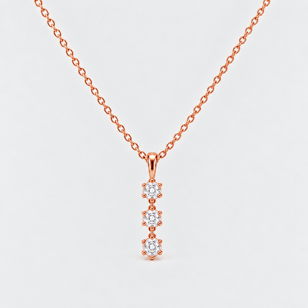A rose gold necklace with a delicate chain and a vertical pendant featuring three small round-cut clear gemstones in prong settings, shown on a light gray background.