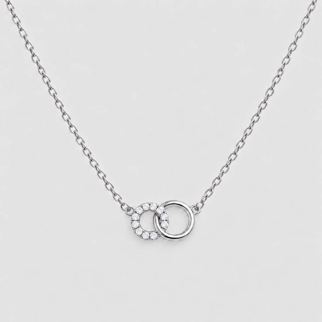 A silver chain necklace featuring a double interlocking ring pendant, with one ring detailed with small clear stones, set against a light gray background.