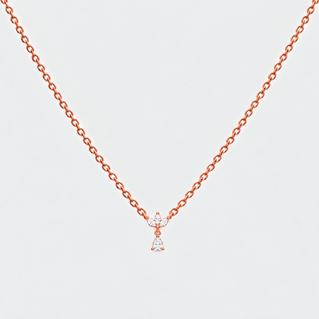 A delicate rose gold chain necklace with a small bow and dangling heart-shaped crystal charm, shown against a light gray background.