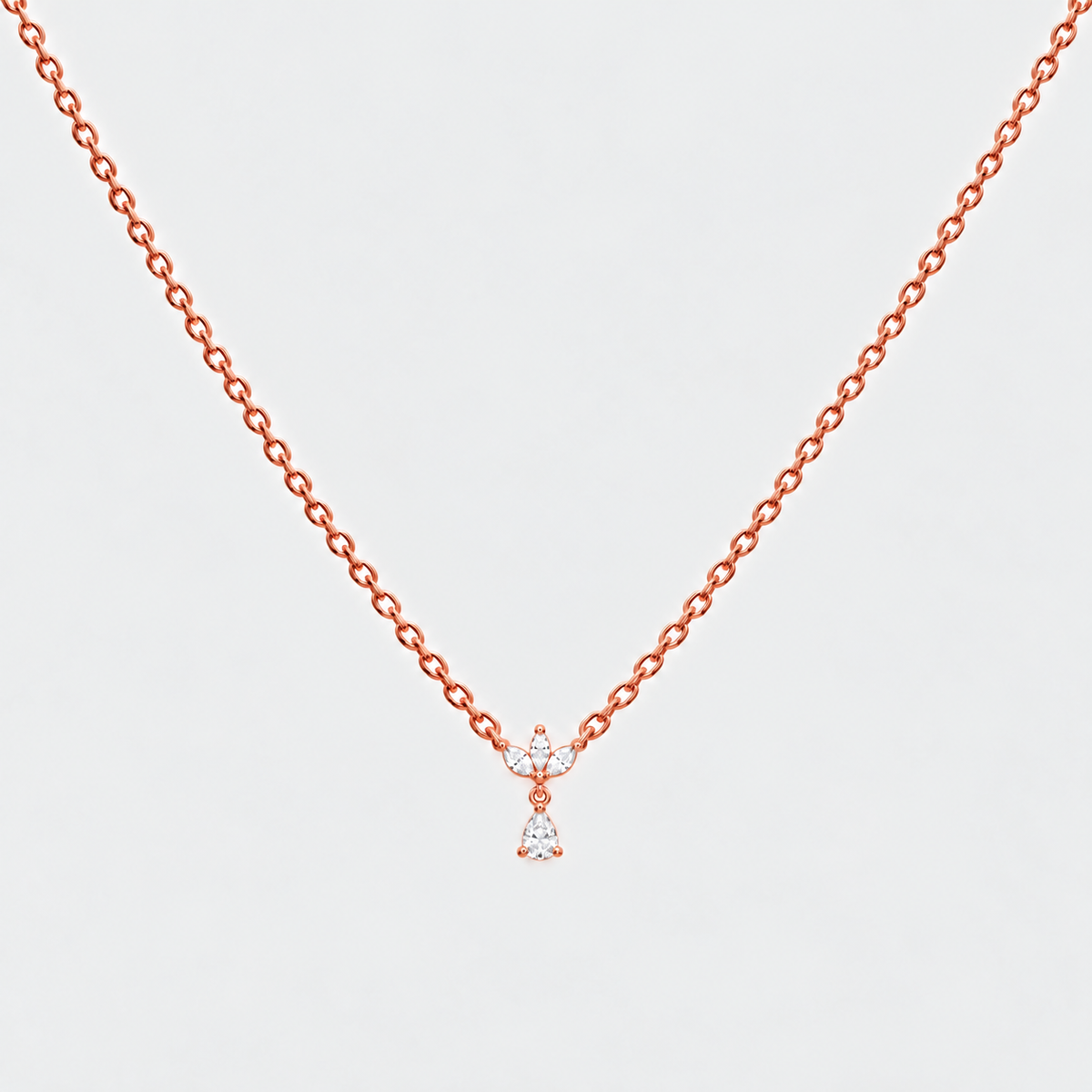 A delicate rose gold chain necklace with a small bow and dangling heart-shaped crystal charm, shown against a light gray background.