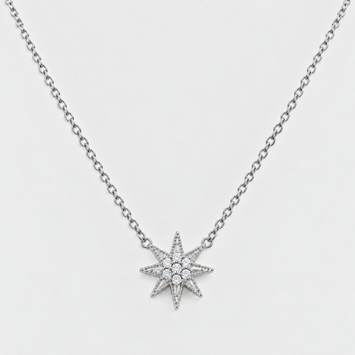 A silver-toned chain necklace featuring a multi-pointed starburst pendant paved with small clear stones, shown against a light gray background.