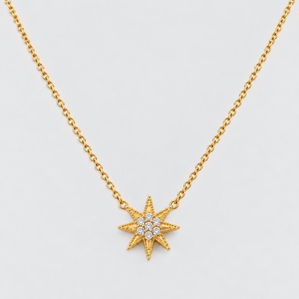 A gold chain necklace featuring a textured eight-pointed star pendant with a small cluster of clear stones in the center, shown against a light gray background.