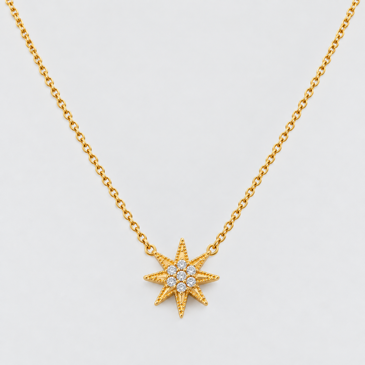 A gold chain necklace featuring a textured eight-pointed star pendant with a small cluster of clear stones in the center, shown against a light gray background.