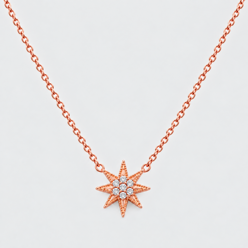 A rose gold necklace with a starburst pendant featuring a central cluster of small clear gemstones, shown against a light gray background.