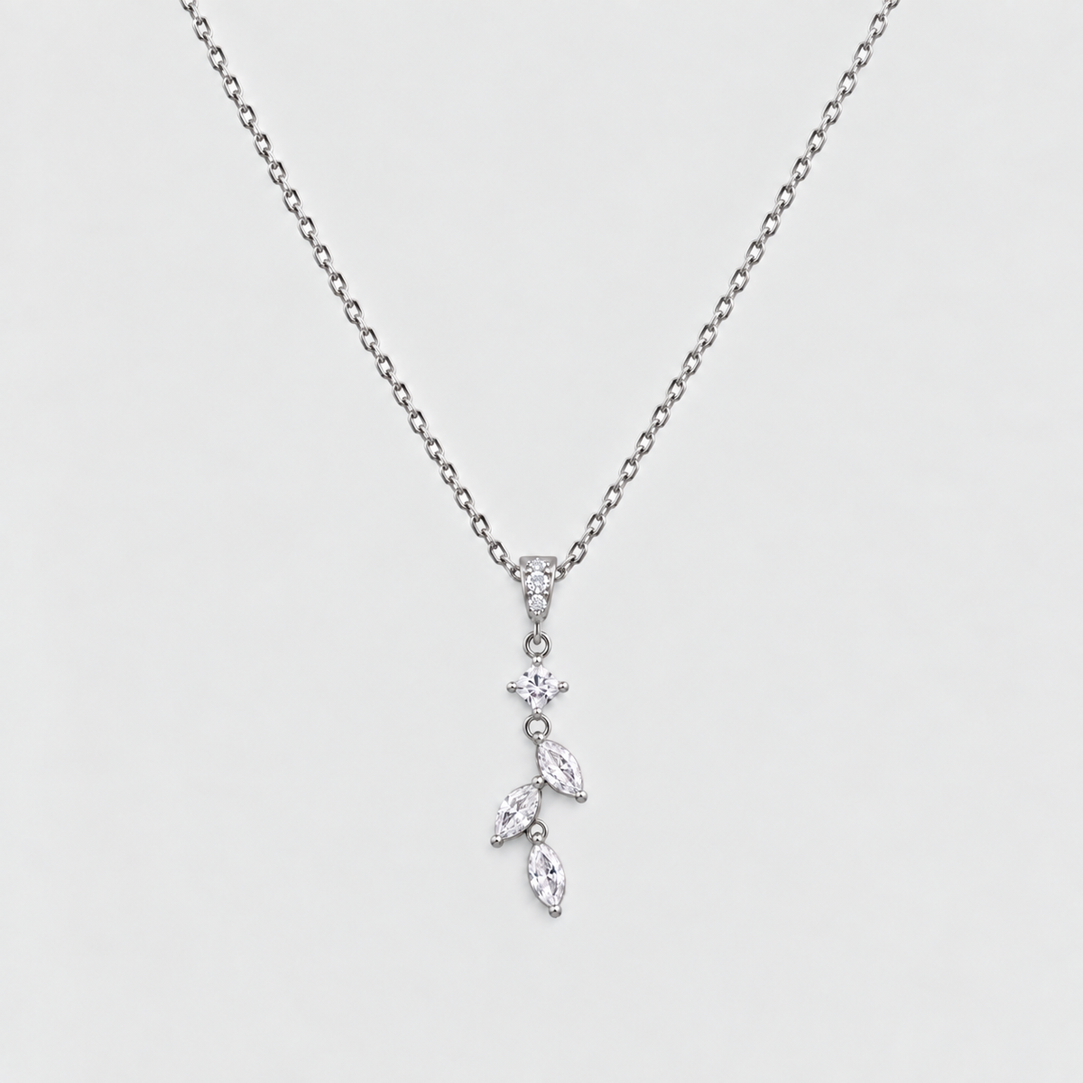 A delicate silver-toned necklace featuring a small floral and leaf pendant set with clear marquise and round-cut stones, displayed against a light gray background.