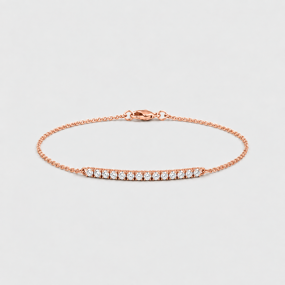 A delicate rose gold chain bracelet with a central bar set with small clear gemstones, displayed on a light gray background.