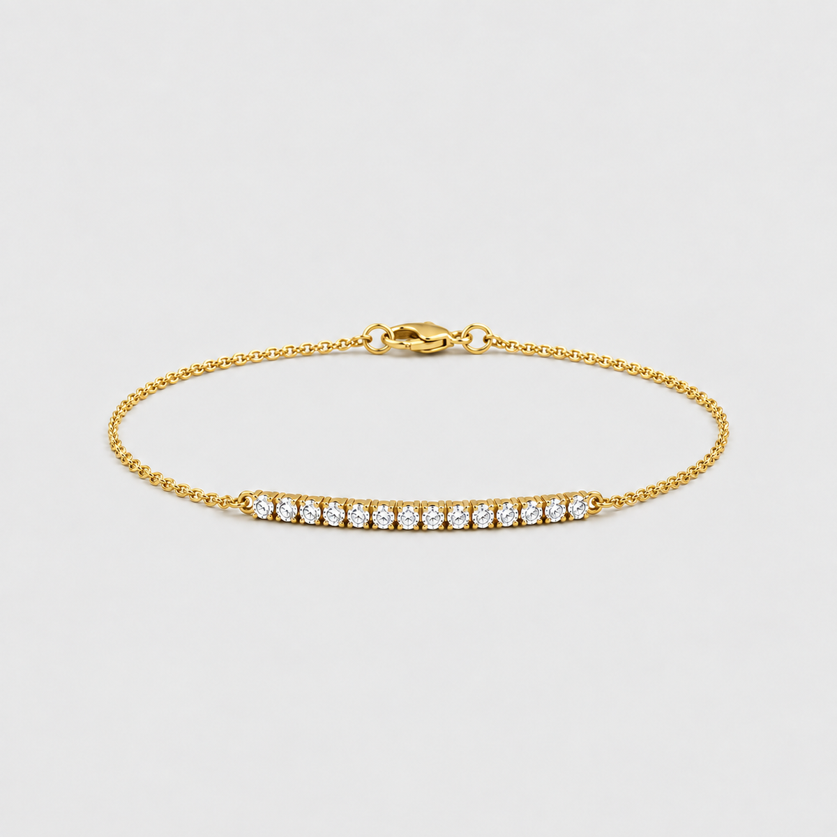 A delicate yellow gold chain bracelet featuring a central bar set with small round clear gemstones, displayed on a light gray background.
