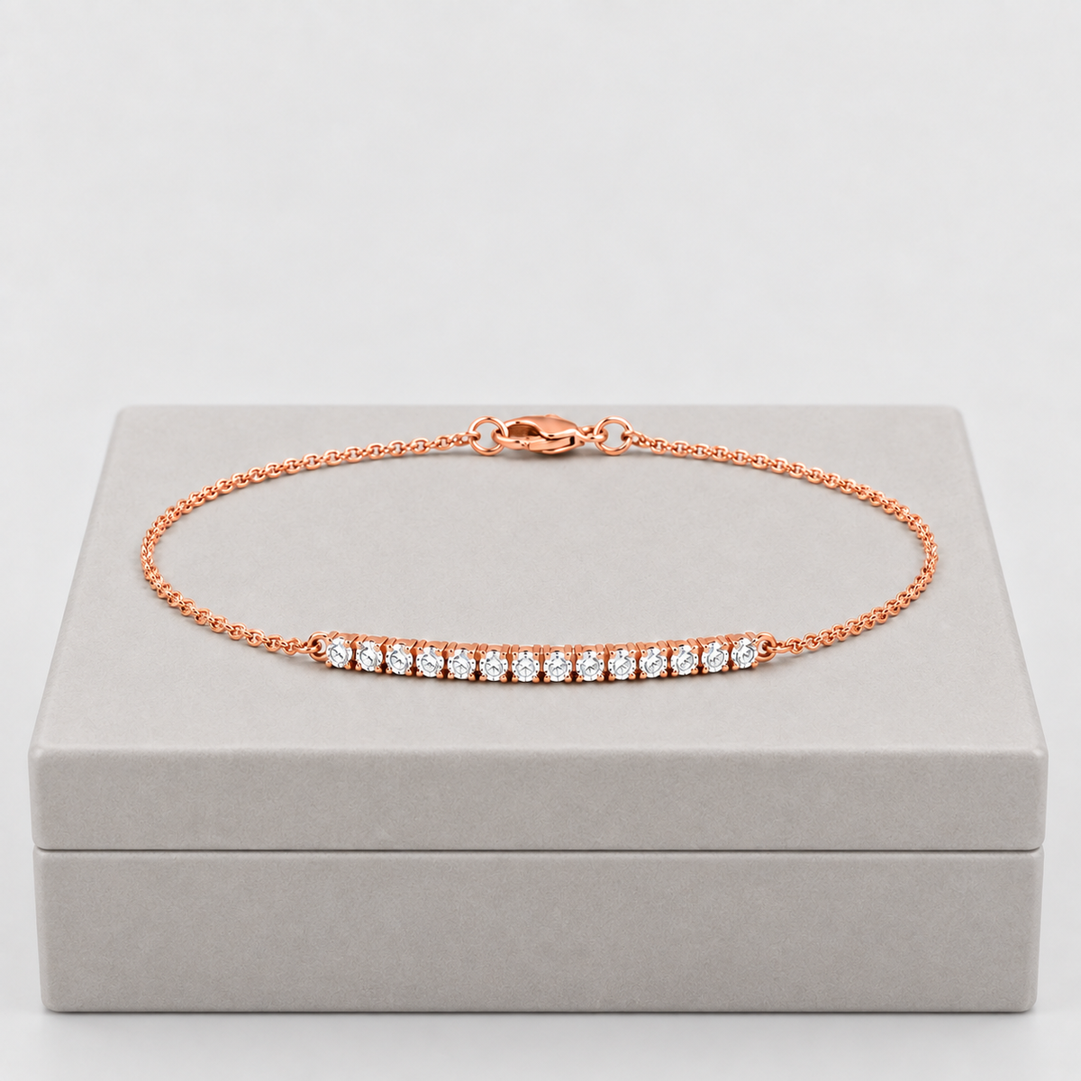 A rose gold chain bracelet with a bar of small clear stones, displayed on a light gray jewelry box against a light gray background.
