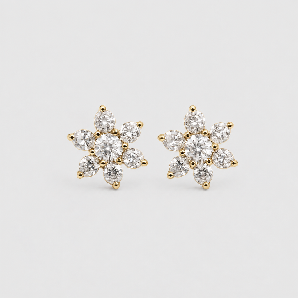 A pair of gold flower-shaped stud earrings set with clear round-cut gemstones, photographed on a clean light gray background.