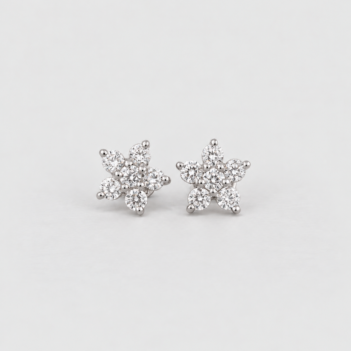 A pair of silver stud earrings shaped like snowflakes, set with small clear cubic zirconia stones, on a light gray background.