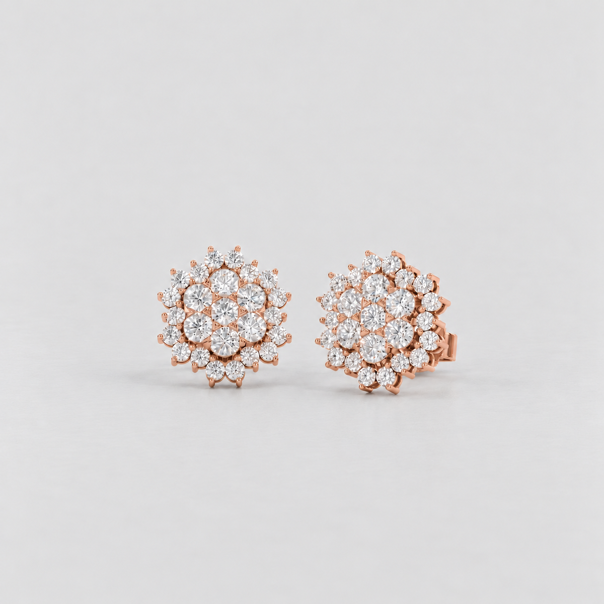 A pair of rose gold stud earrings featuring round-cut clear gemstones arranged in a floral or snowflake-like cluster pattern, set against a clean light gray background.