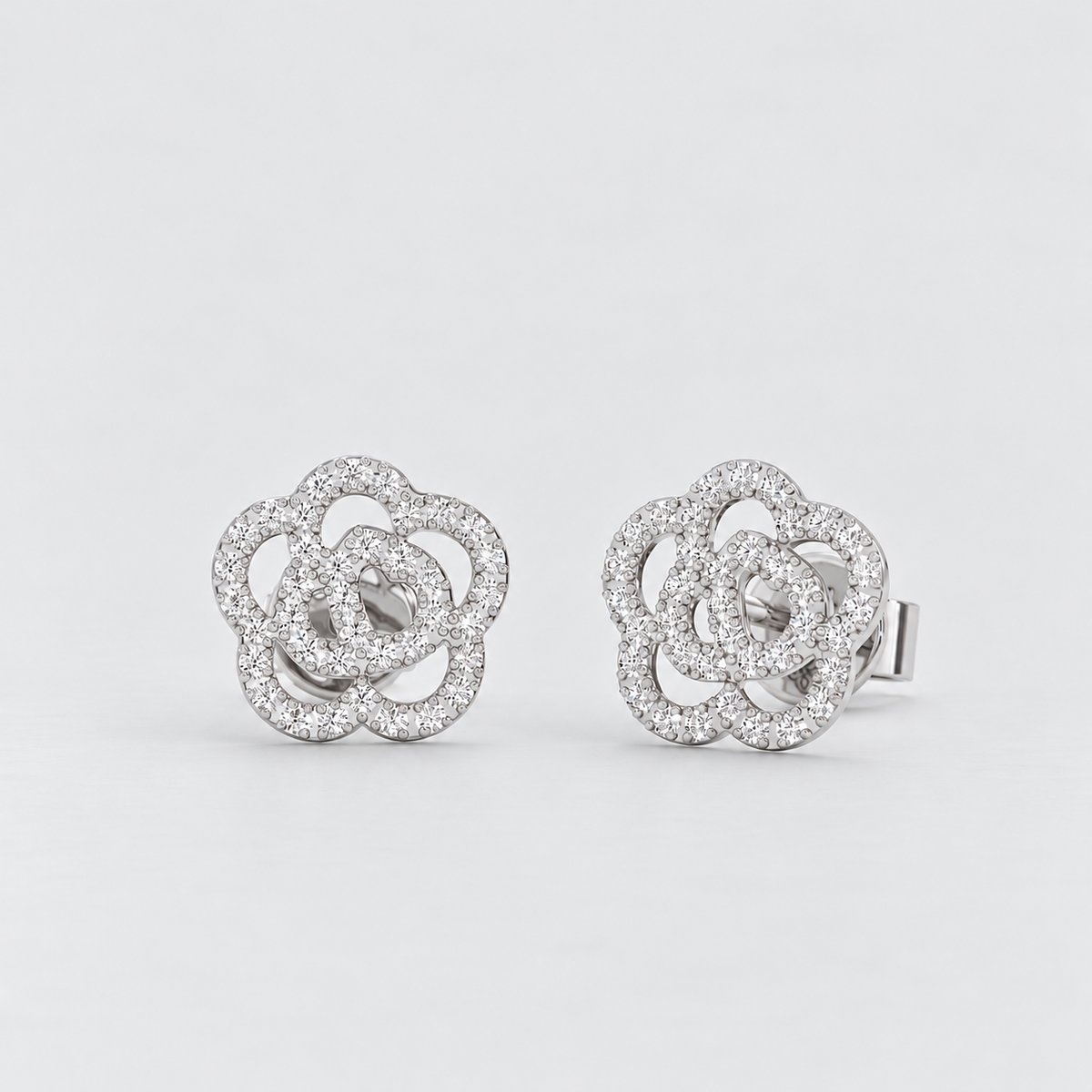A pair of silver-toned interlocking flower stud earrings paved with small clear stones, shown on a light gray background.