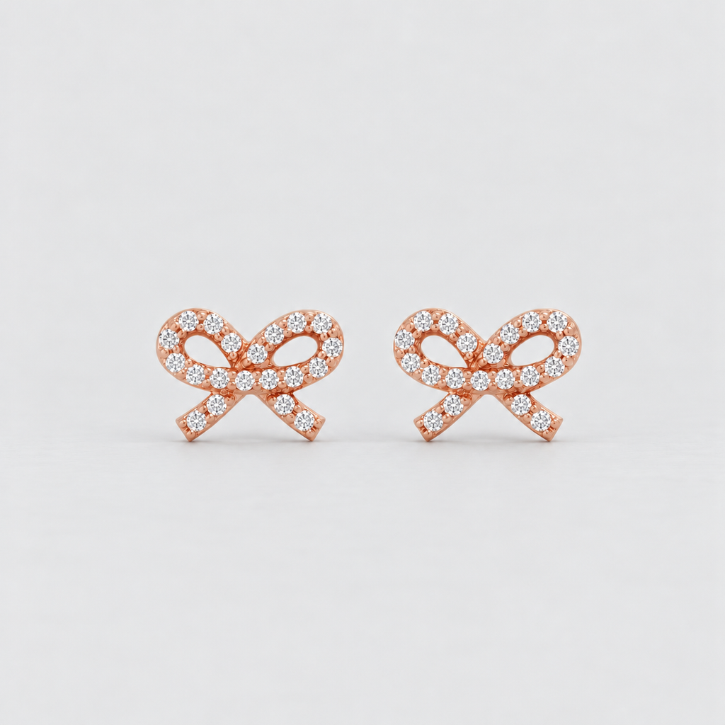 A pair of rose gold bow-shaped stud earrings paved with small clear gemstones, set against a clean light gray background.