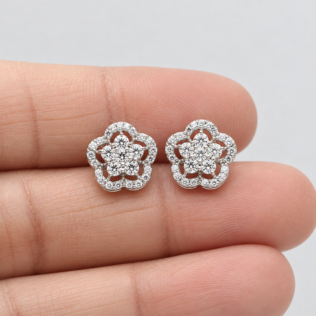 Pair of flower-shaped diamond cluster stud earrings in white gold held on a person's hand.
