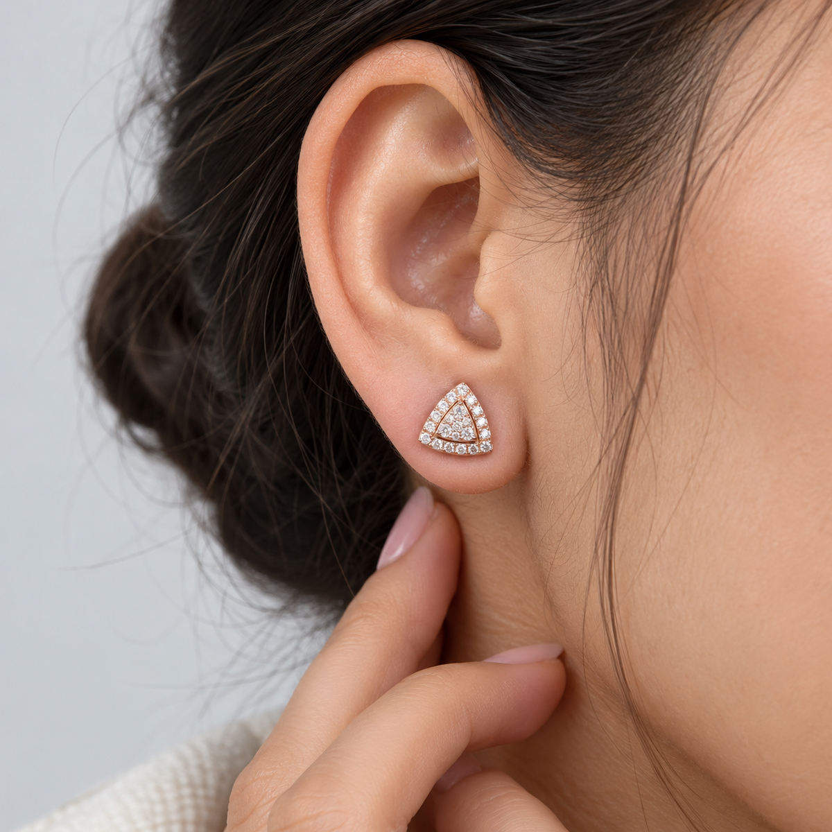 Close-up of a woman wearing a cluster diamond stud earring in a triangular gold setting.

