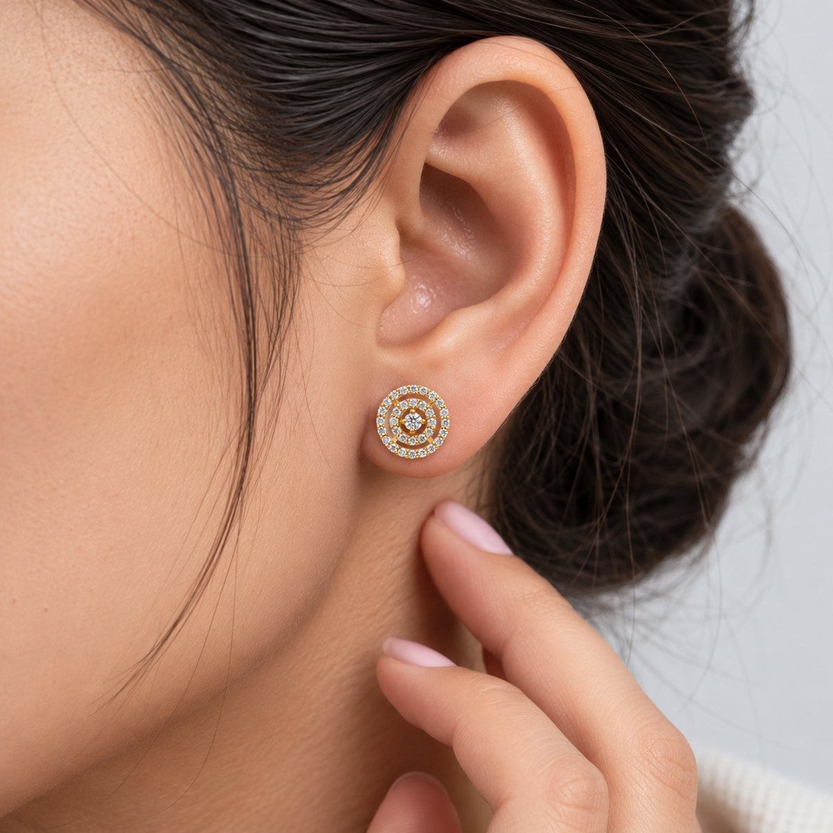 Round cluster diamond halo stud earrings in yellow gold worn by a woman.