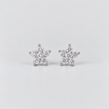 A pair of silver stud earrings shaped like snowflakes, each adorned with small clear round-cut gemstones, set against a plain light gray background.