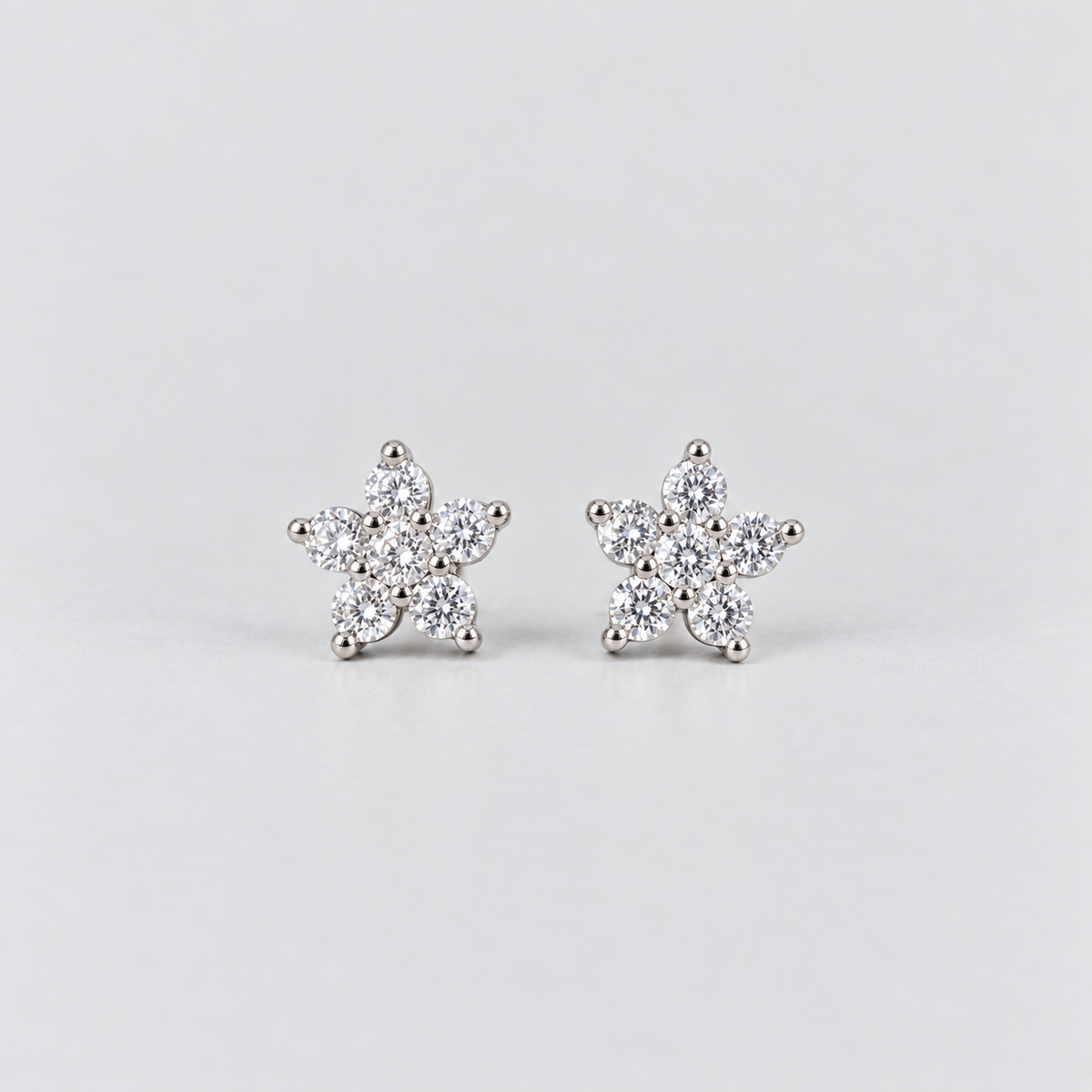 A pair of silver stud earrings shaped like snowflakes, each adorned with small clear round-cut gemstones, set against a plain light gray background.