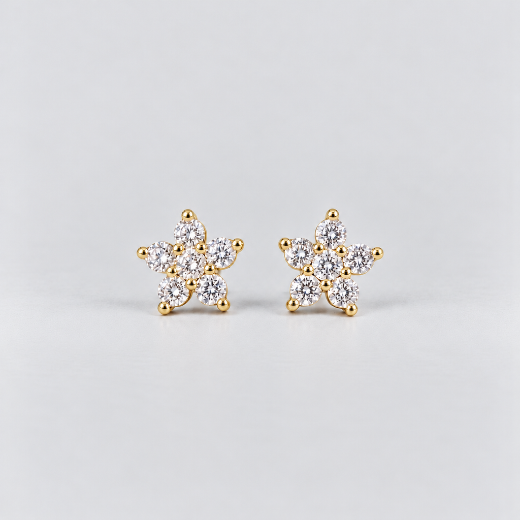 A pair of gold flower-shaped stud earrings set with clear round-cut gemstones, photographed on a clean light gray background.