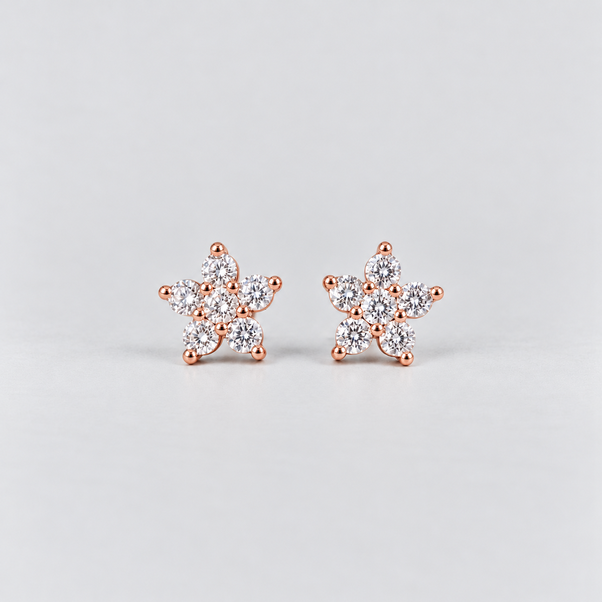 A pair of rose gold stud earrings with a snowflake or flower-like design set with clear gemstones, displayed on a light gray background.