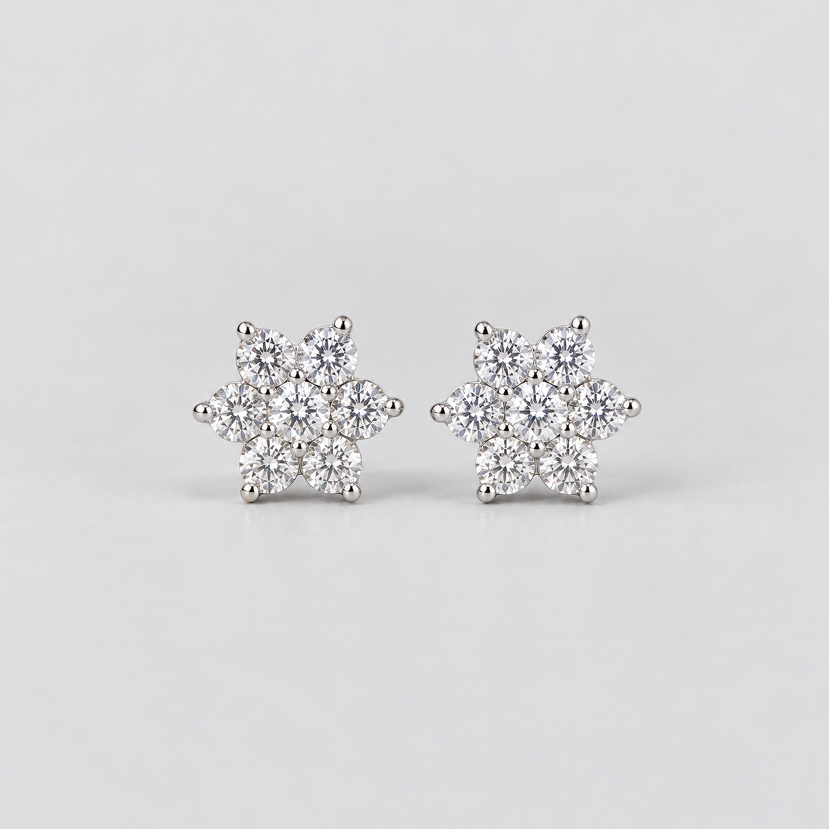 A pair of snowflake-shaped stud earrings made of silver metal and clear gemstones, set against a plain light gray background.