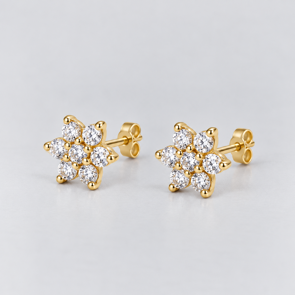 A pair of gold stud earrings featuring a cluster of round-cut clear gemstones in a flower-like arrangement, set on a light gray background.