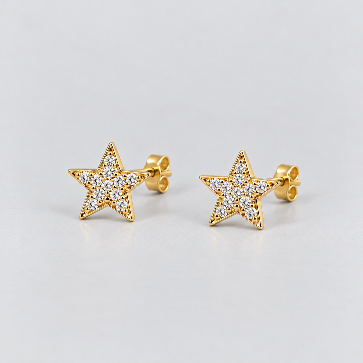 A pair of gold star-shaped stud earrings paved with small clear stones, shown on a light gray background.
