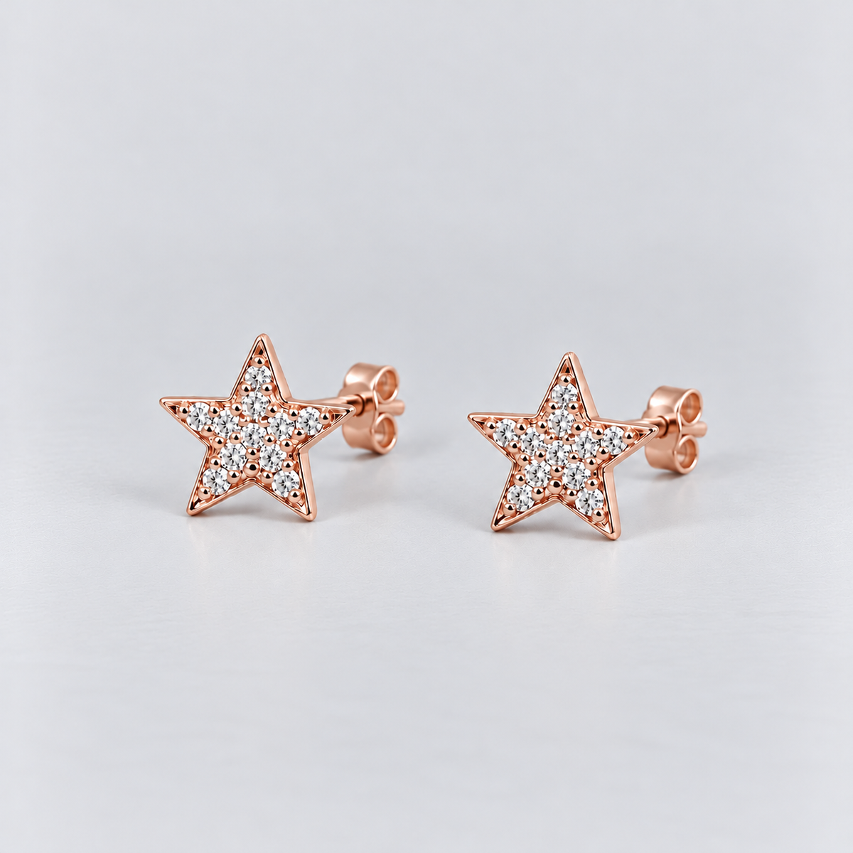 A pair of rose gold star-shaped stud earrings paved with small clear stones, displayed on a light gray background.
