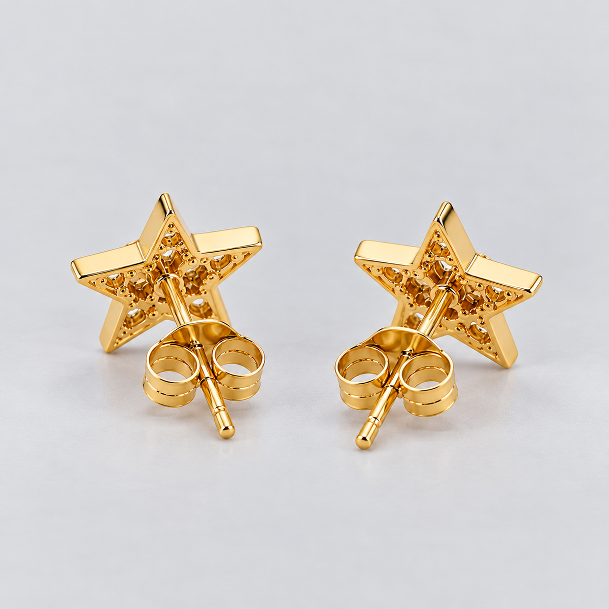 A pair of gold star-shaped stud earrings shown from the back, displaying the butterfly clutch backings, on a light gray background.