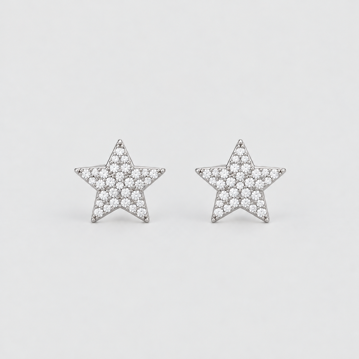 A pair of star-shaped stud earrings paved with small clear stones in a silver-tone setting, displayed on a clean light gray background.